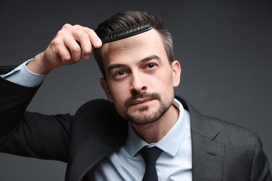 Handsome businessman combing his hair on dark background