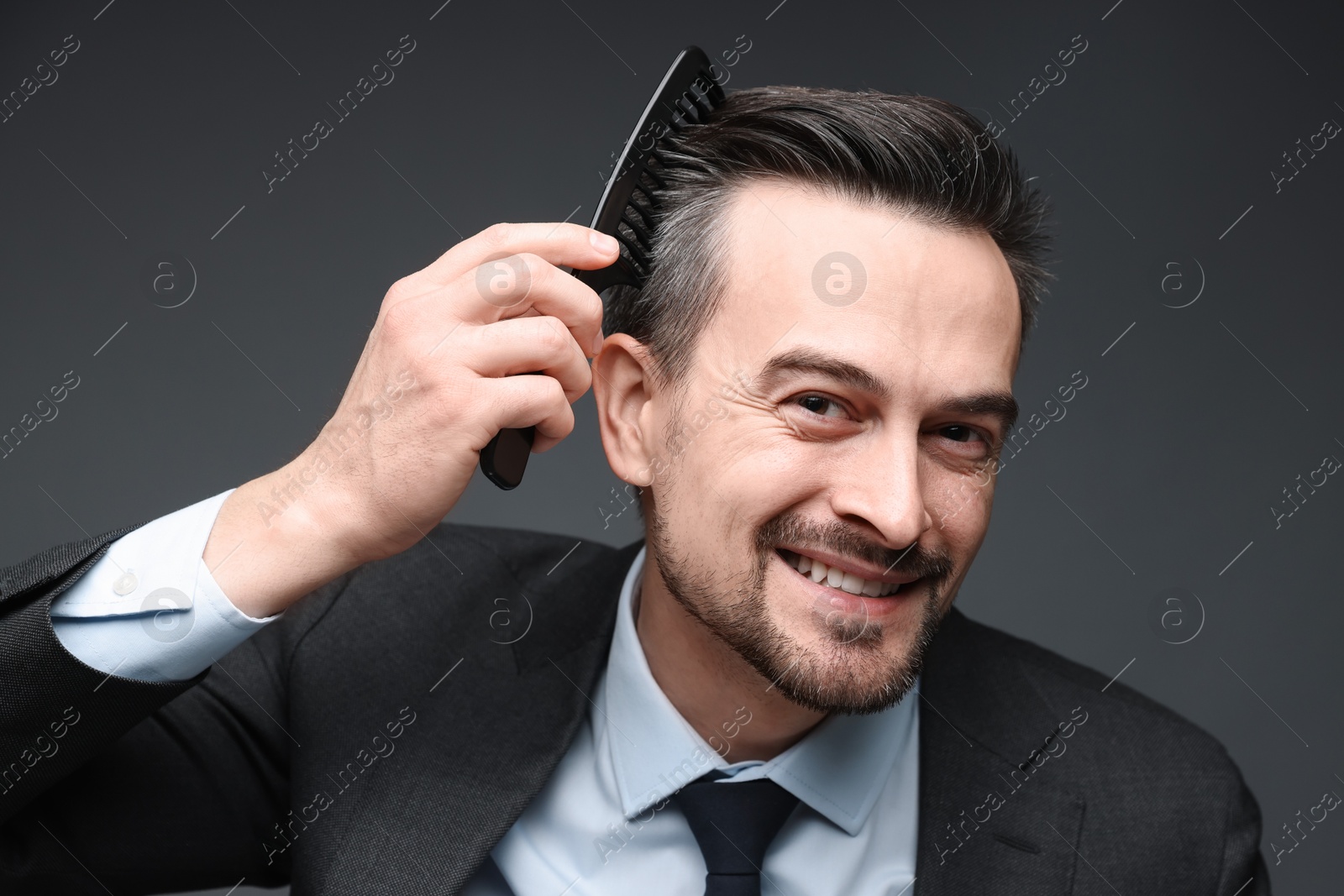 Photo of Handsome businessman combing his hair on dark background