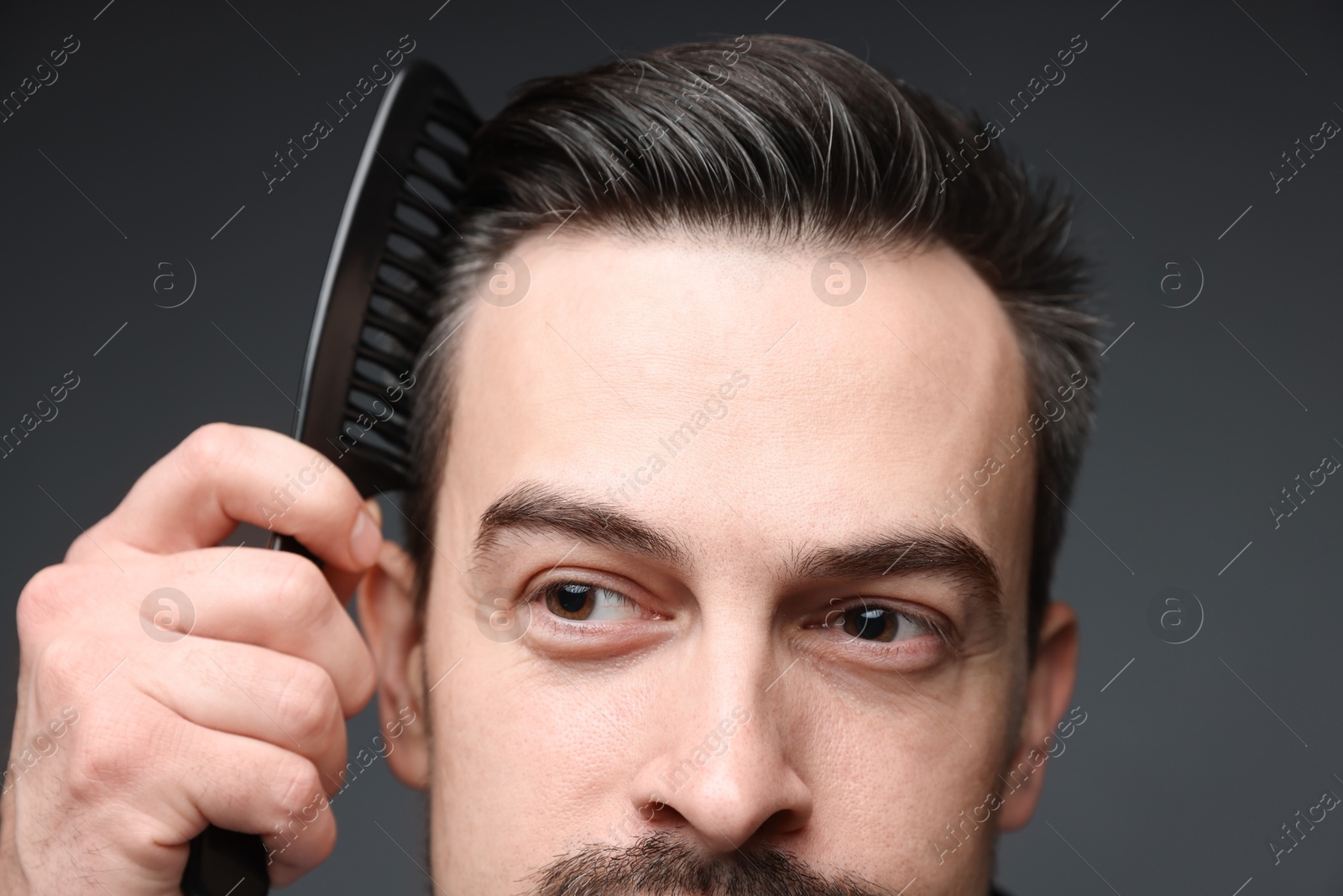 Photo of Handsome man combing his hair on dark background, closeup