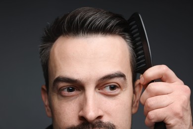 Photo of Handsome man combing his hair on dark background, closeup