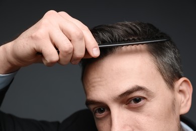 Photo of Handsome man combing his hair on dark background, closeup