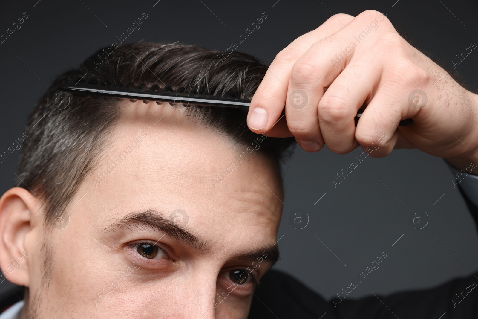 Photo of Handsome man combing his hair on dark background, closeup