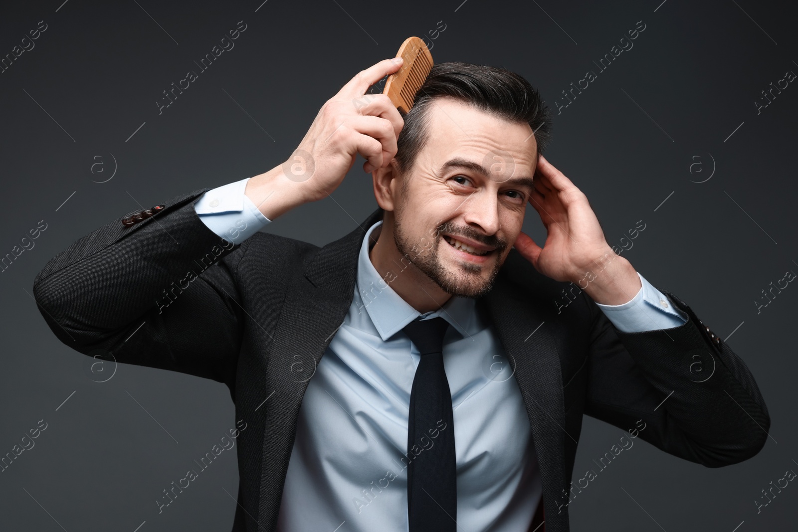 Photo of Handsome businessman combing his hair on dark background