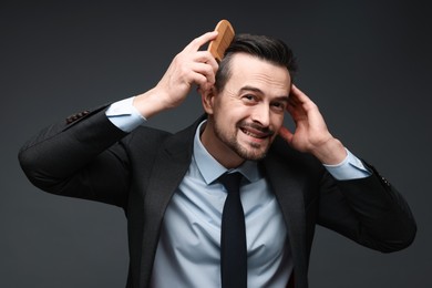 Handsome businessman combing his hair on dark background