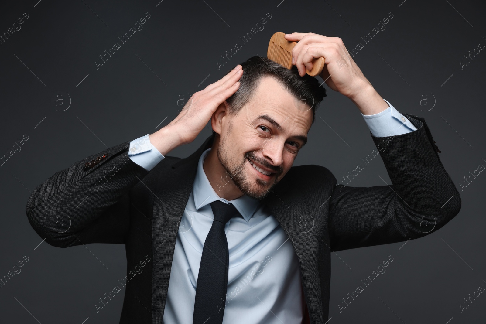 Photo of Handsome businessman combing his hair on dark background