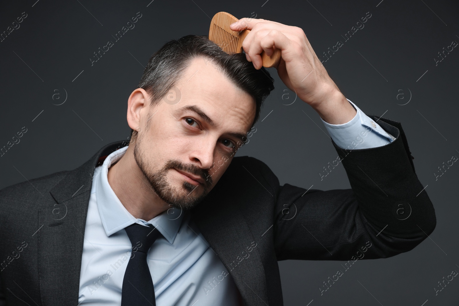 Photo of Handsome businessman combing his hair on dark background