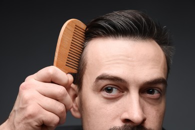 Photo of Handsome man combing his hair on dark background, closeup