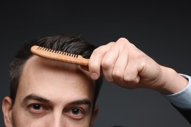 Photo of Handsome man combing his hair on dark background, closeup