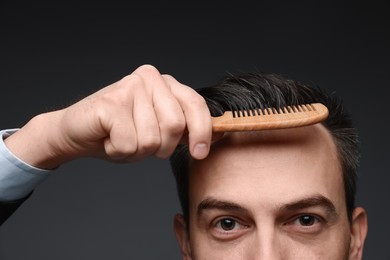 Handsome man combing his hair on dark background, closeup