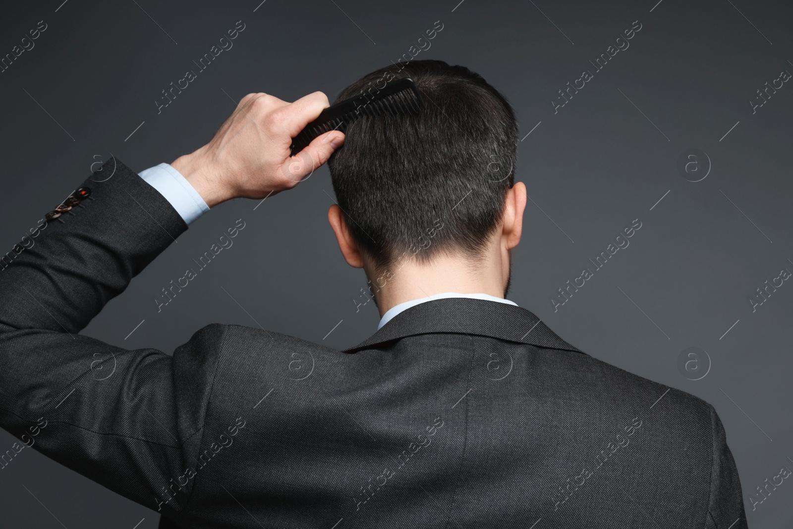 Photo of Man combing his hair on dark background, back view