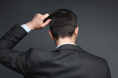 Photo of Man combing his hair on dark background, back view