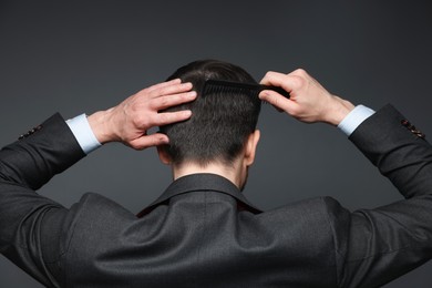 Photo of Man combing his hair on dark background, back view