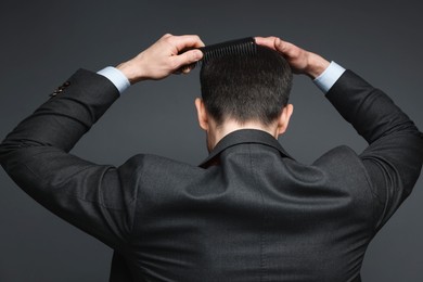 Photo of Man combing his hair on dark background, back view