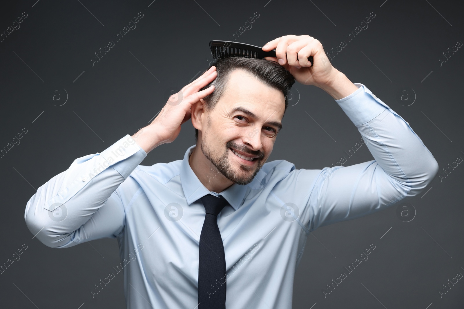 Photo of Handsome man combing his hair on dark background