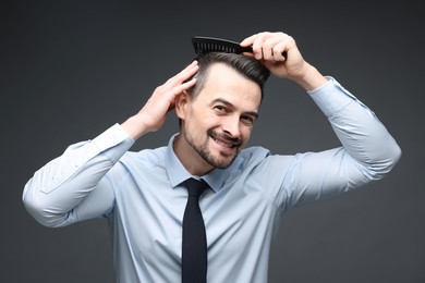 Photo of Handsome man combing his hair on dark background