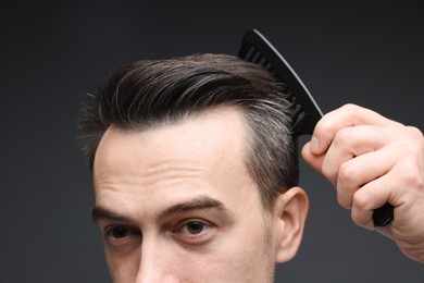 Photo of Handsome man combing his hair on dark background, closeup