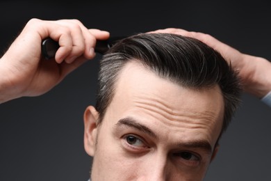 Handsome man combing his hair on dark background, closeup