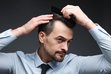 Photo of Handsome man combing his hair on dark background