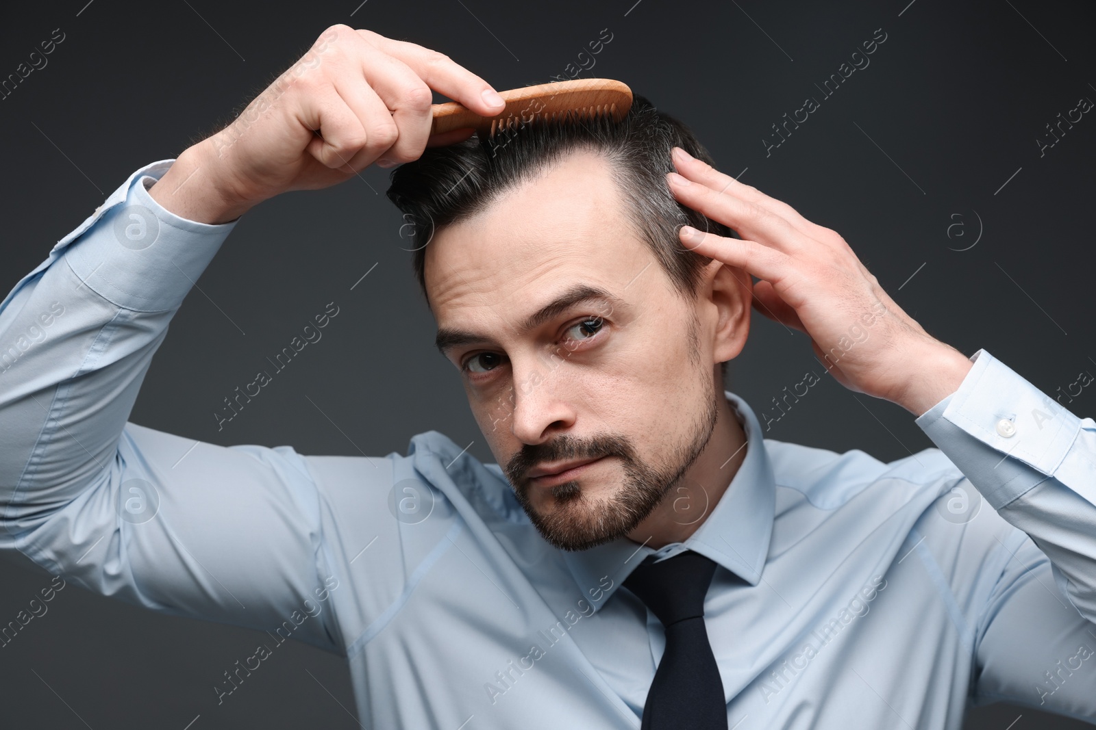 Photo of Handsome man combing his hair on dark background