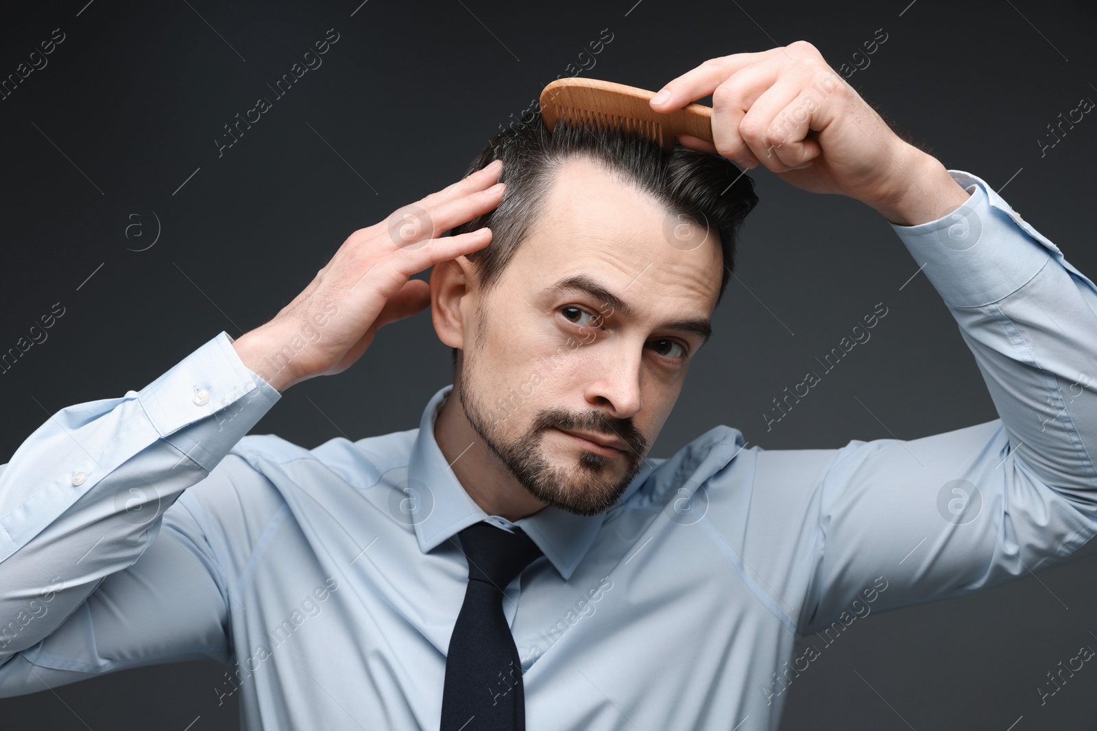 Photo of Handsome man combing his hair on dark background