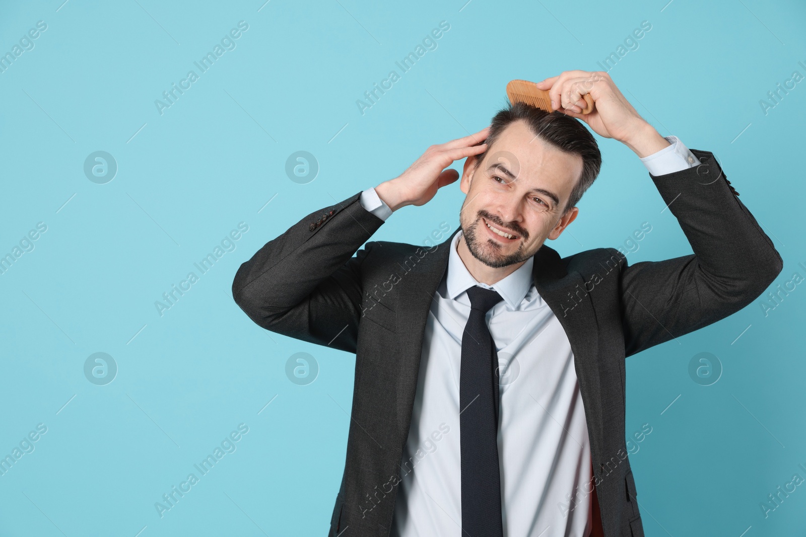 Photo of Handsome man stylish his hair with comb on light blue background