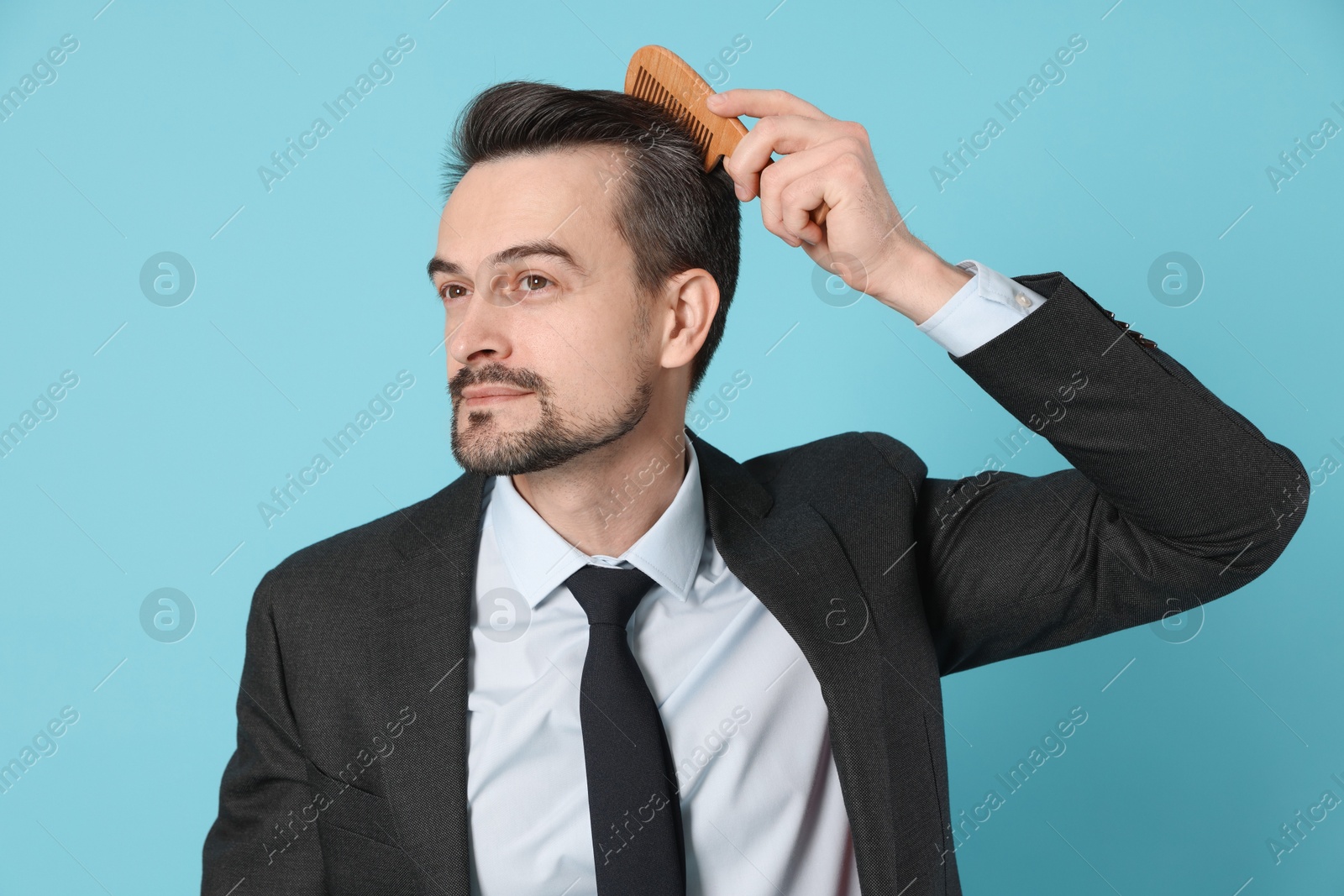 Photo of Handsome man stylish his hair with comb on light blue background