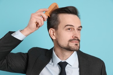 Photo of Handsome man stylish his hair with comb on light blue background