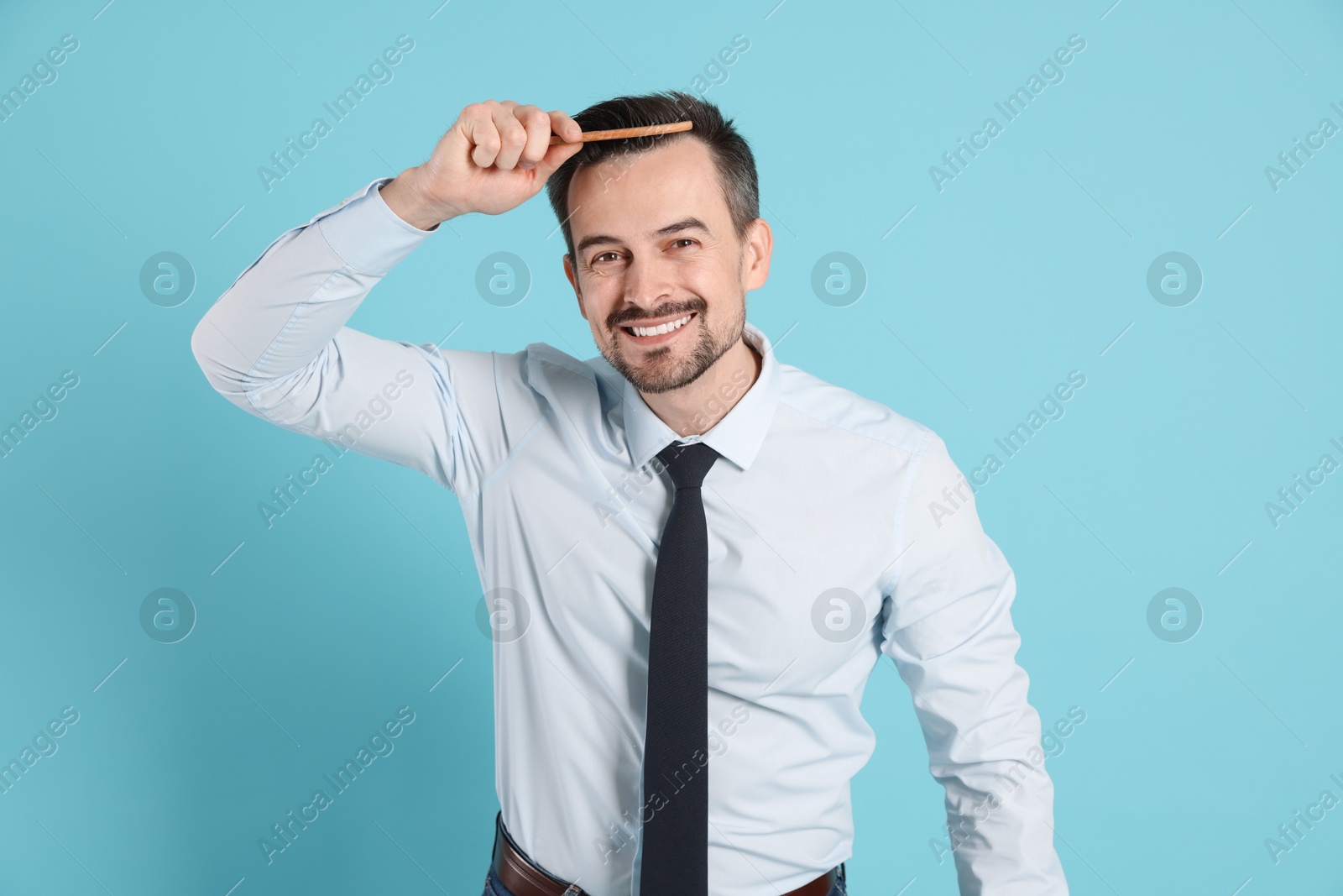 Photo of Handsome man stylish his hair with comb on light blue background