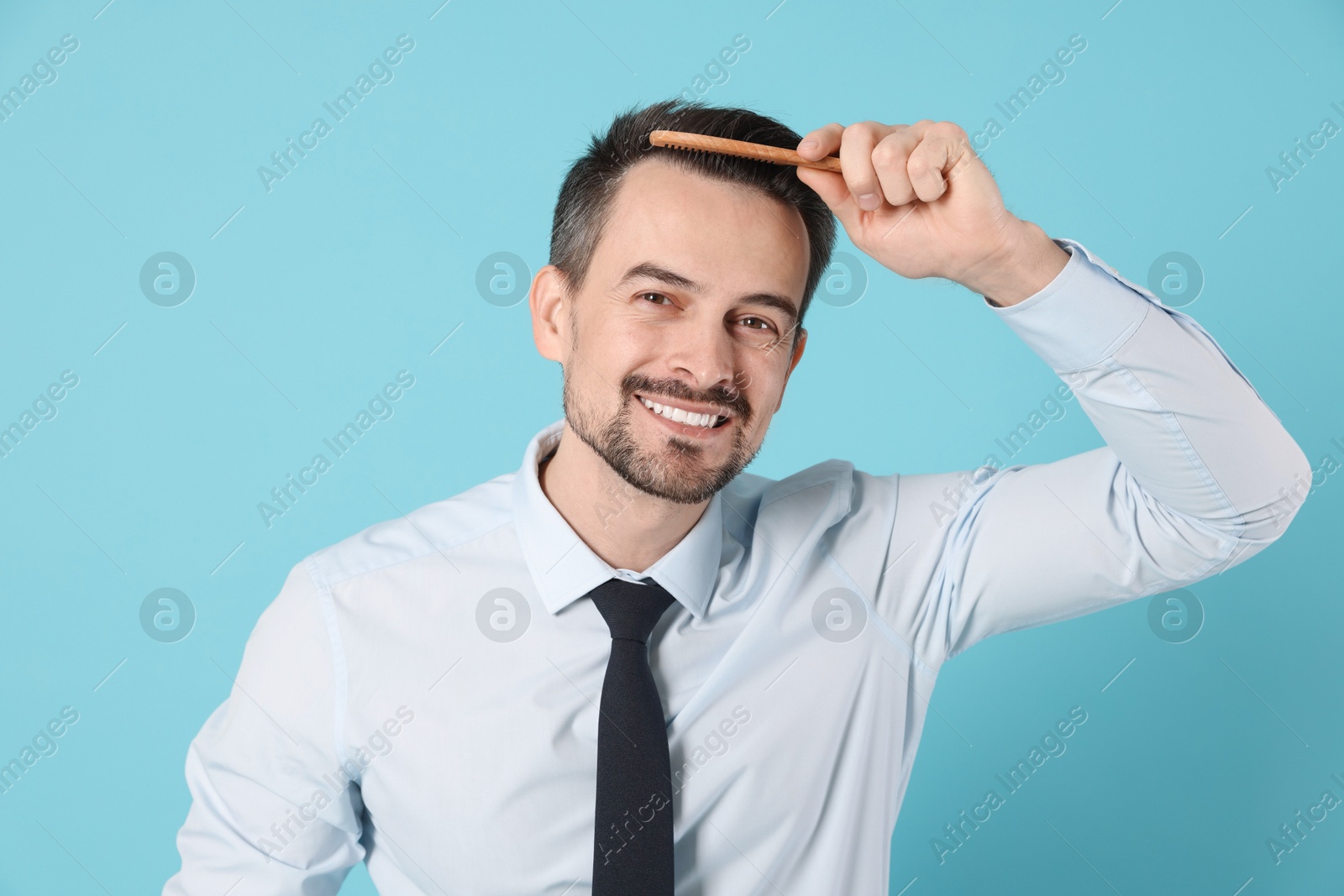 Photo of Handsome man stylish his hair with comb on light blue background