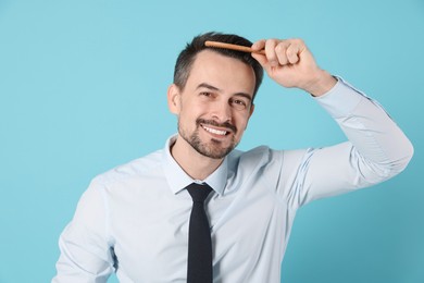 Photo of Handsome man stylish his hair with comb on light blue background