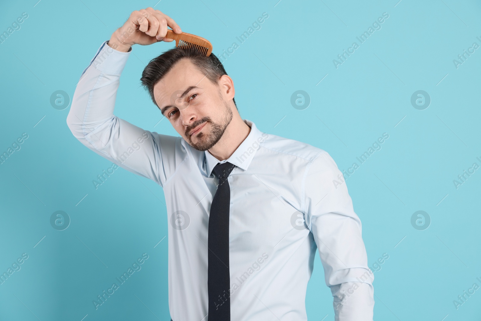 Photo of Handsome man stylish his hair with comb on light blue background