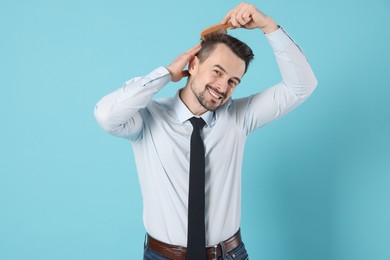 Handsome man stylish his hair with comb on light blue background