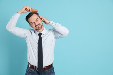 Handsome man stylish his hair with comb on light blue background