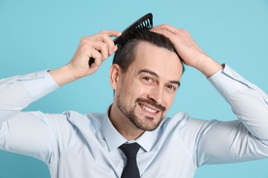 Photo of Handsome man stylish his hair with comb on light blue background