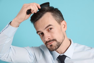 Photo of Handsome man stylish his hair with comb on light blue background