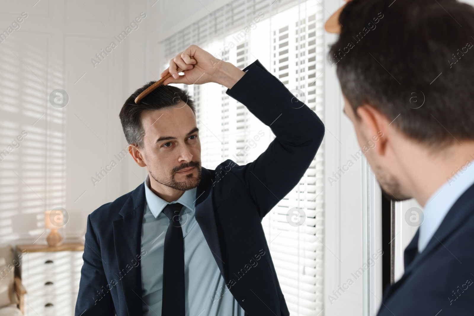 Photo of Handsome man styling his hair with comb near mirror at home