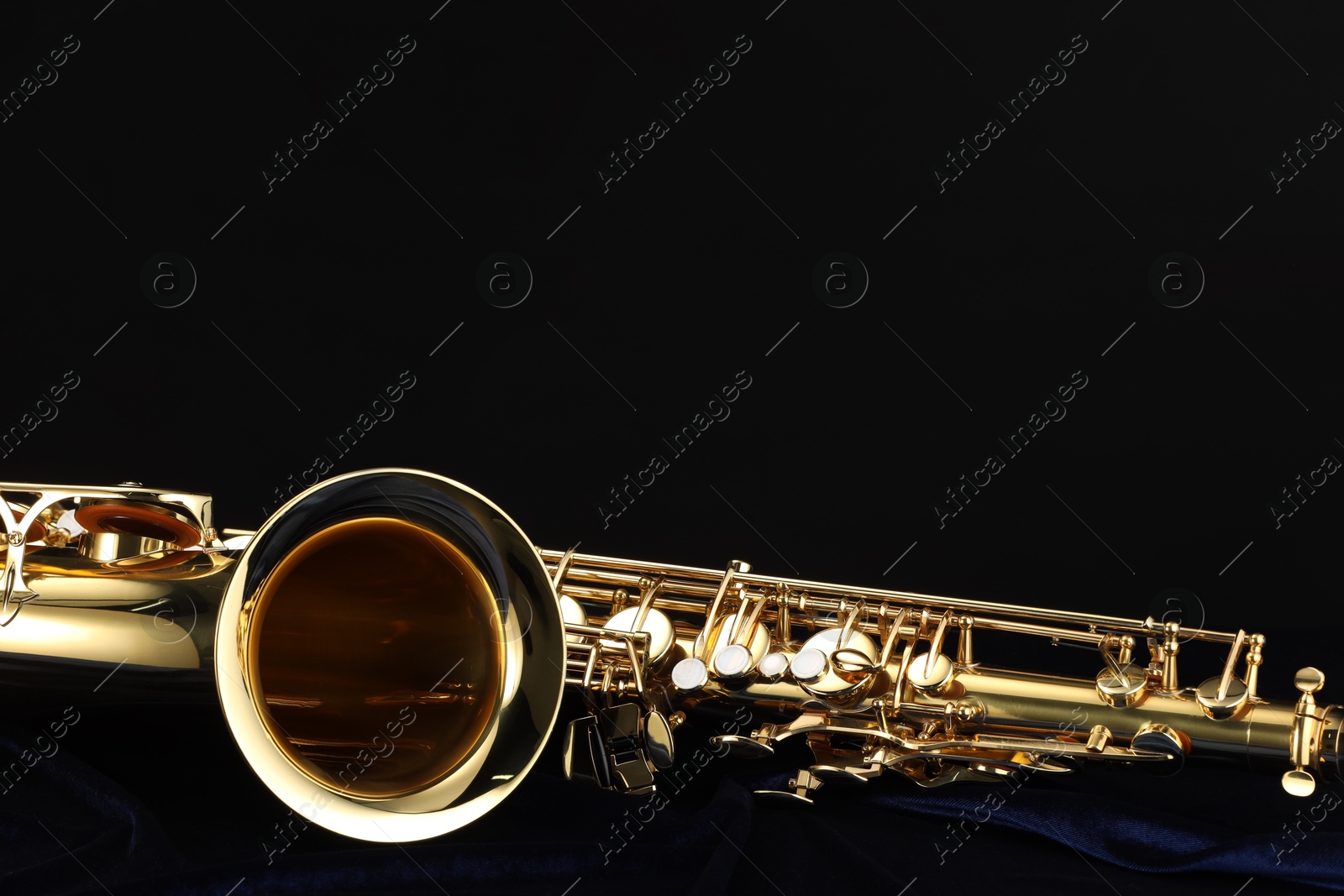 Photo of Jazz. One beautiful saxophone on dark blue fabric against black background, closeup. Space for text