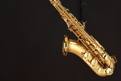 Photo of Jazz. One beautiful saxophone hanging from strap on black background, space for text