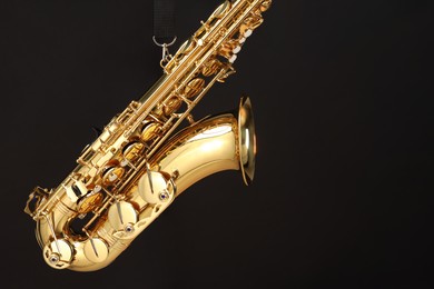 Photo of Jazz. One beautiful saxophone hanging from strap on black background, space for text