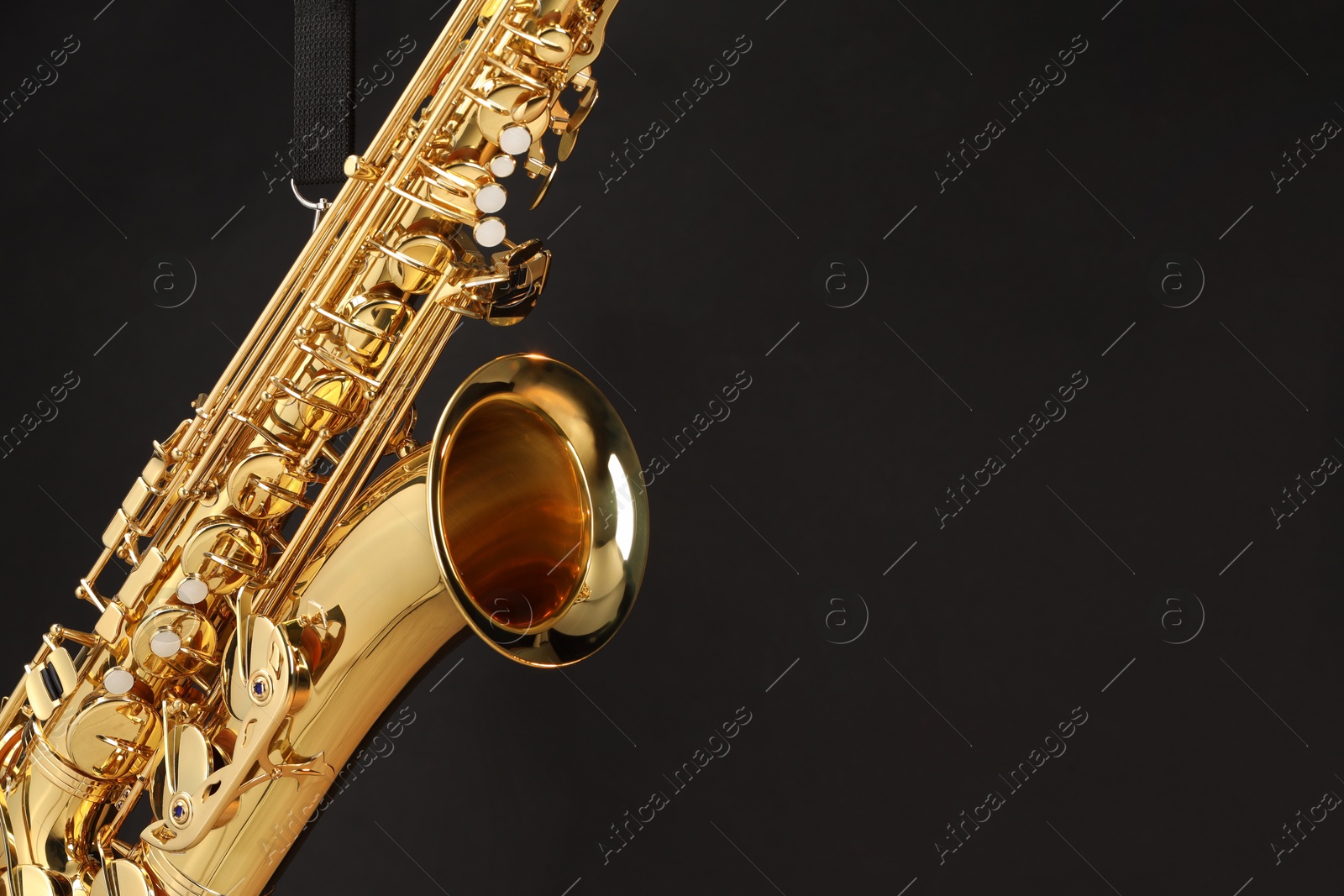 Photo of Jazz. One beautiful saxophone hanging from strap on black background, closeup. Space for text