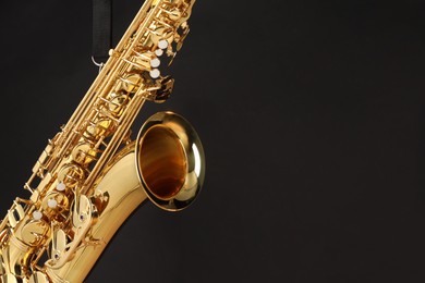 Photo of Jazz. One beautiful saxophone hanging from strap on black background, closeup. Space for text