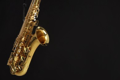 Photo of Jazz. One beautiful saxophone hanging from strap on black background, space for text