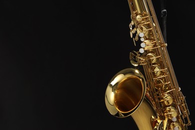 Photo of Jazz. One beautiful saxophone hanging from strap on black background, closeup. Space for text