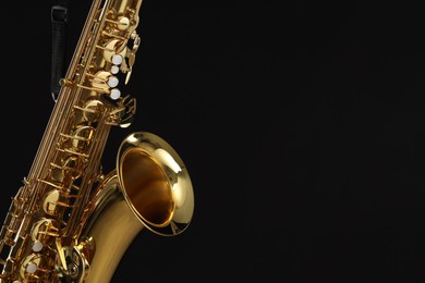 Photo of Jazz. One beautiful saxophone hanging from strap on black background, closeup. Space for text