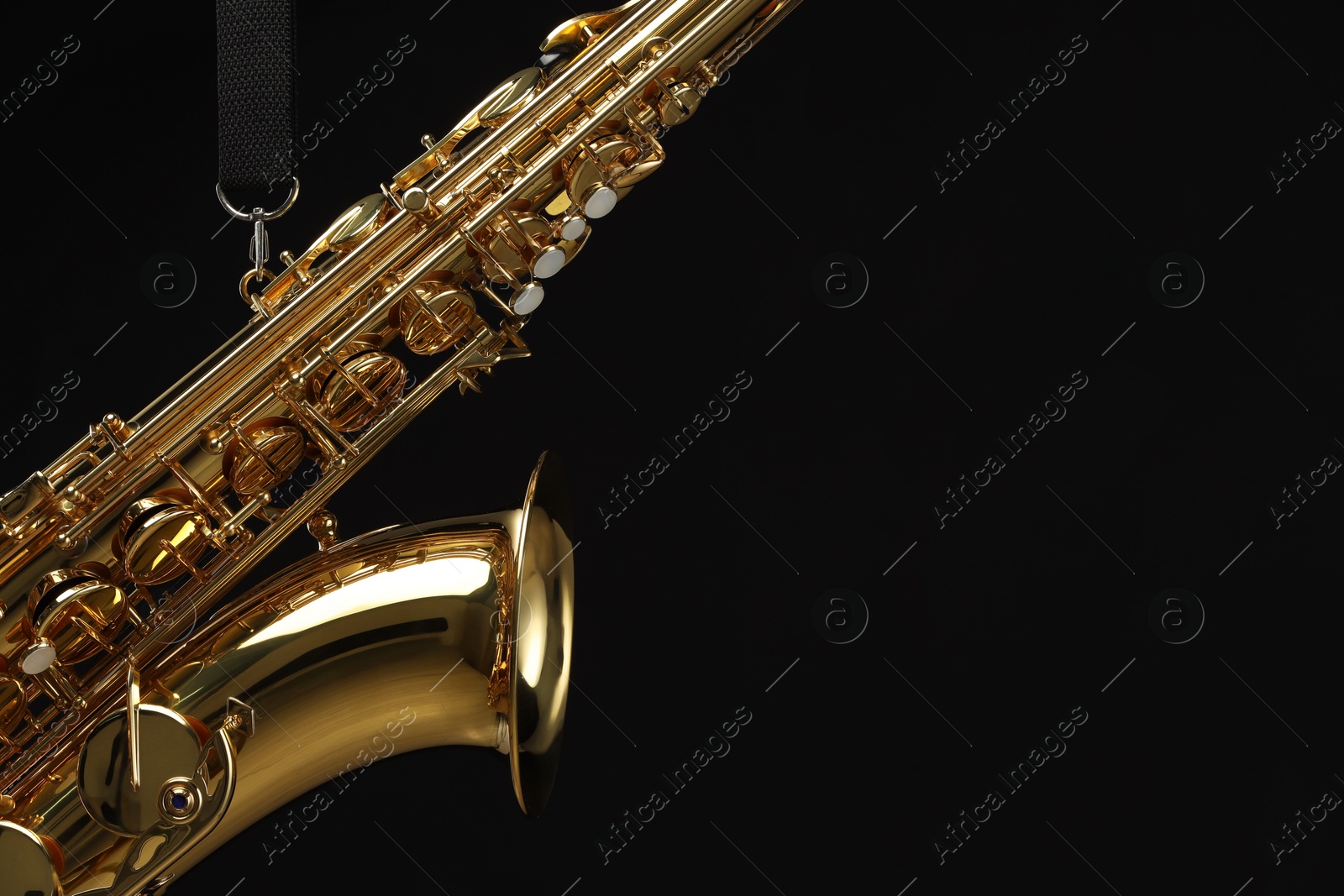 Photo of Jazz. One beautiful saxophone hanging from strap on black background, closeup. Space for text