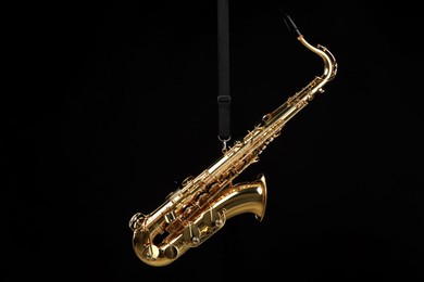 Photo of Jazz. One beautiful saxophone hanging from strap on black background