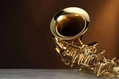 Photo of Jazz. One beautiful saxophone on light grey table against brown background, closeup. Space for text