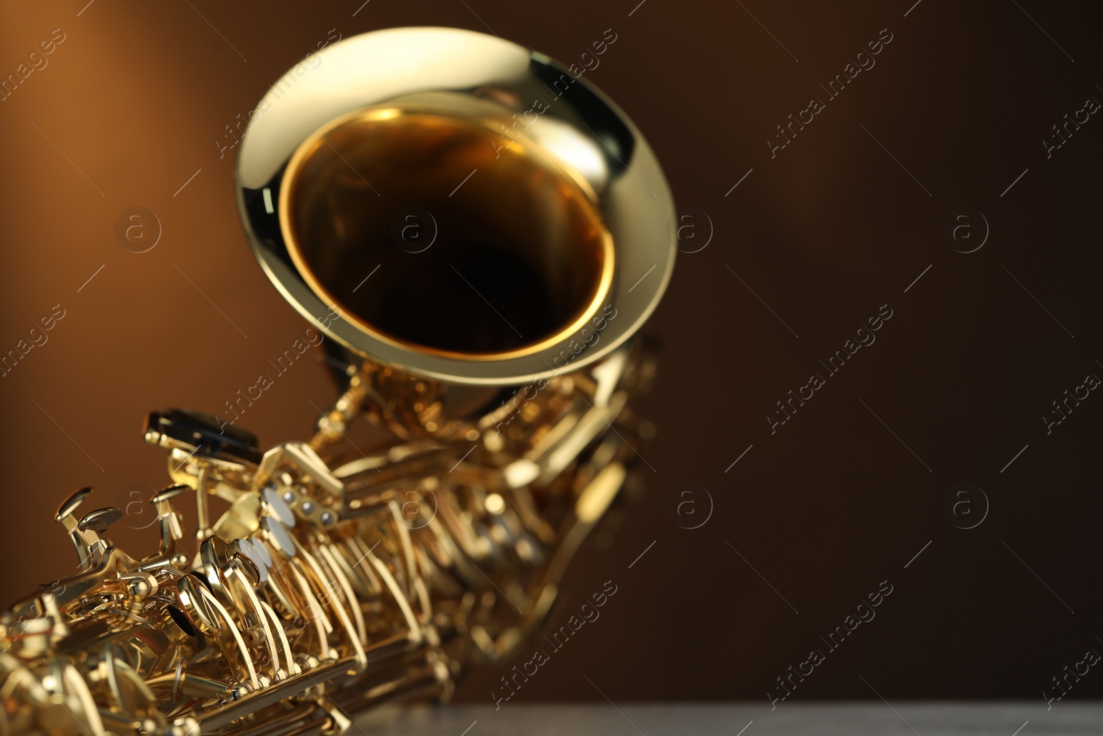 Photo of Jazz. One beautiful saxophone on light grey table against brown background, closeup. Space for text