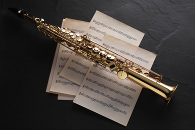 Photo of Jazz. Saxophone and music notes on black table, top view