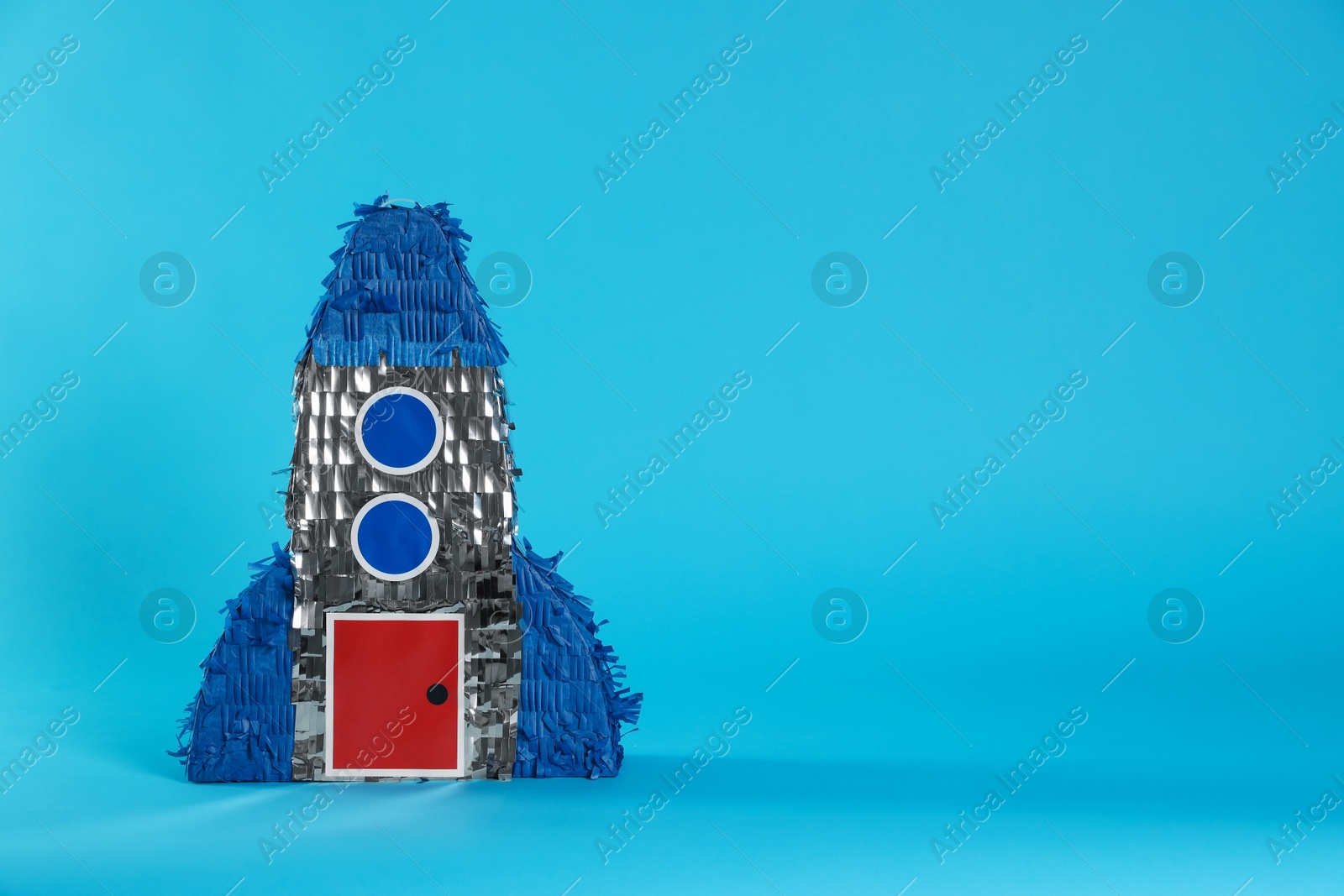 Photo of Rocket shaped pinata on light blue background, space for text